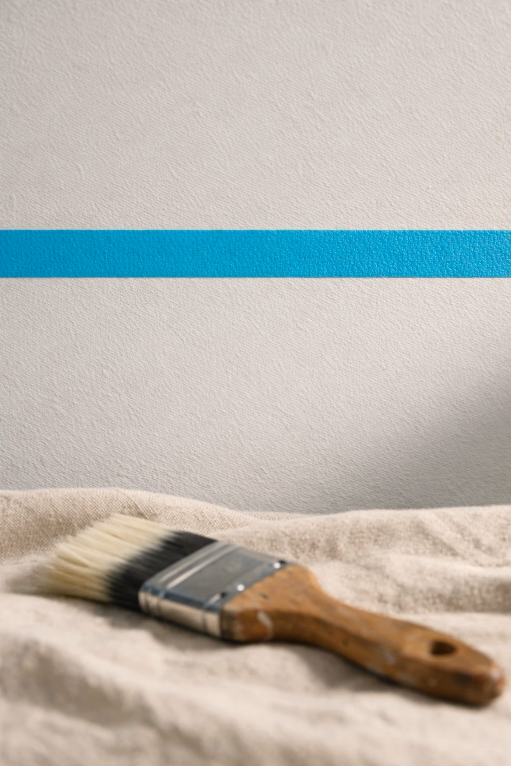 Détail macro d'un ruban de masquage cyan soigneusement aligné à la jonction mur-plafond — signature de la coupe Renovhome