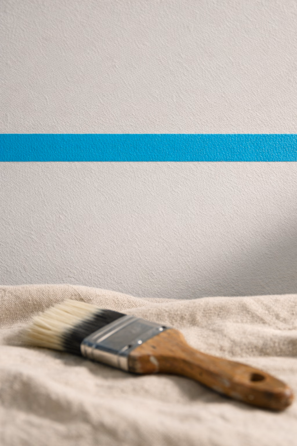 Détail macro d'un ruban de masquage cyan soigneusement aligné à la jonction mur-plafond — signature de la coupe Renovhome