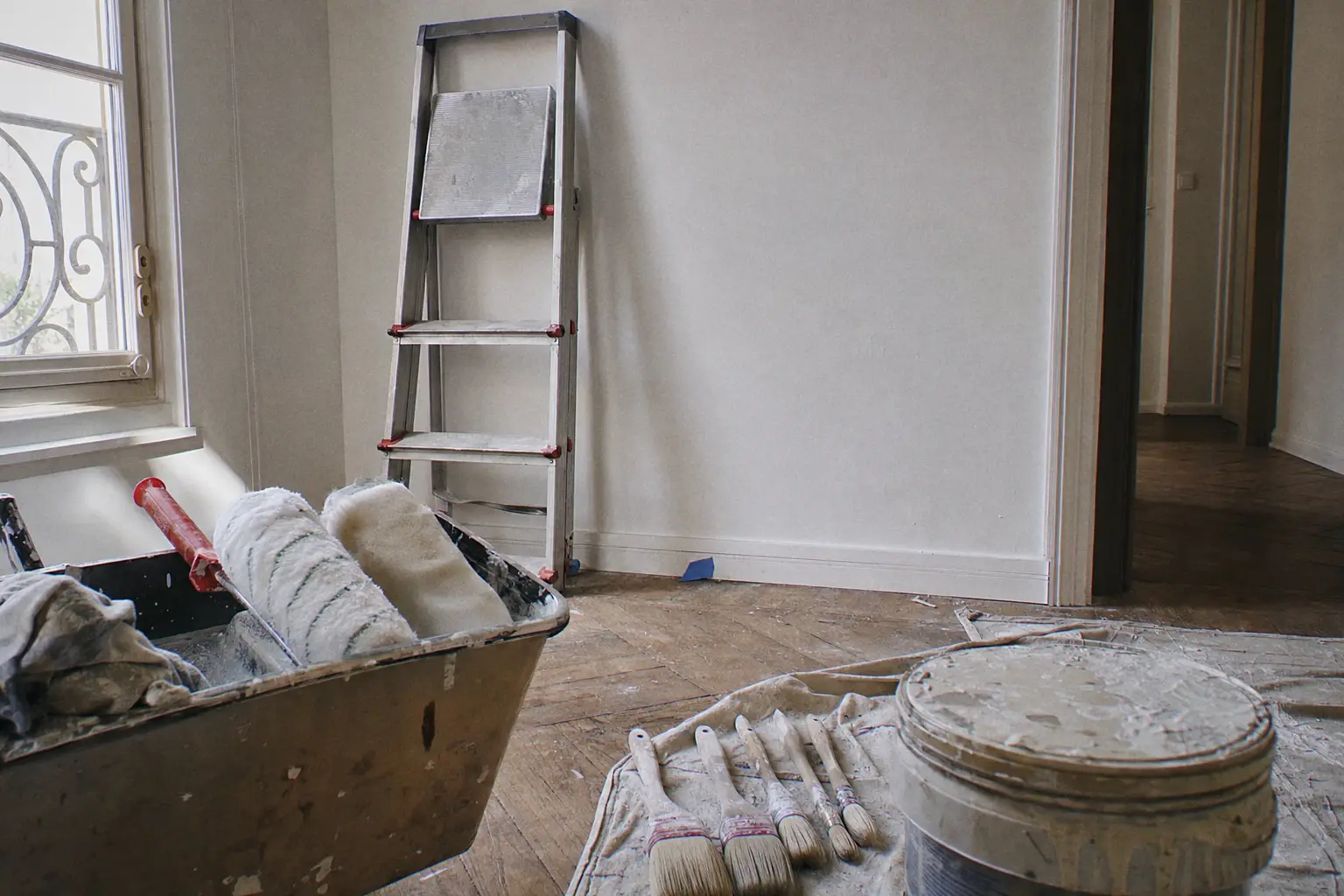 Fin de journée sur un chantier : rouleaux dans le bac, pinceaux nettoyés sur une bâche, escabeau replié contre un mur fraîchement peint