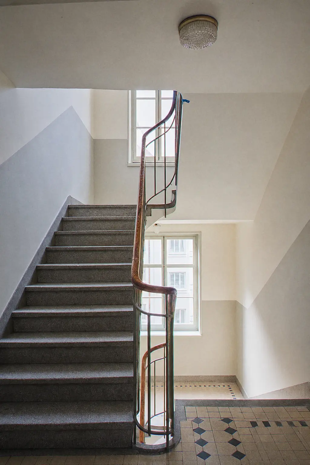 Cage d’escalier d’immeuble genevois repeinte en deux tons, main courante en bois, marches en granit