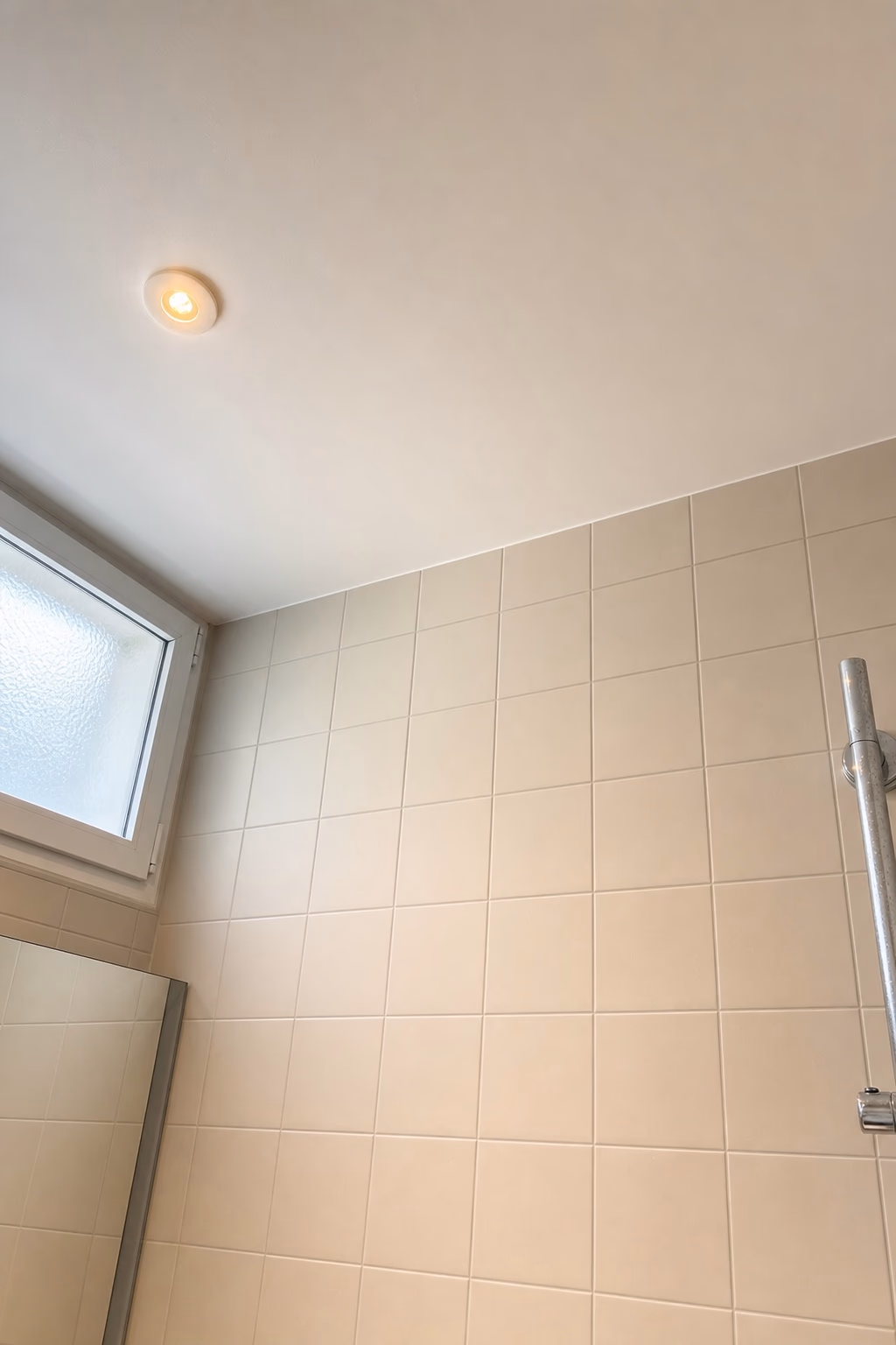Plafond de salle de bains fraîchement repeint en blanc mat à Genève, jonction nette avec la faïence murale claire, spot encastré et imposte vitrée. Chantier Renovhome SA.
