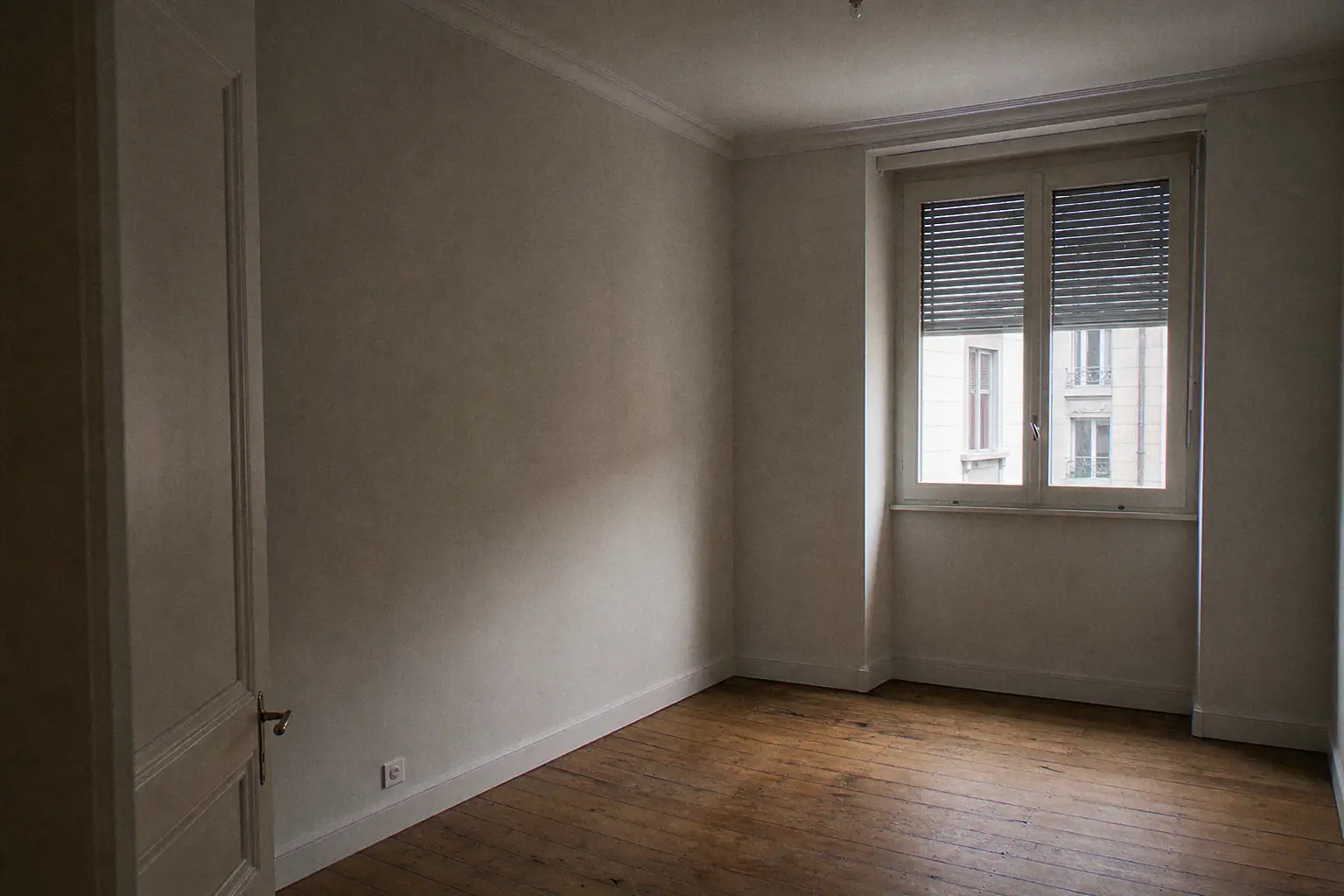 Chambre vide rafraîchie : murs gris perle doux, porte ancienne repeinte en émail blanc, parquet en chêne d'origine