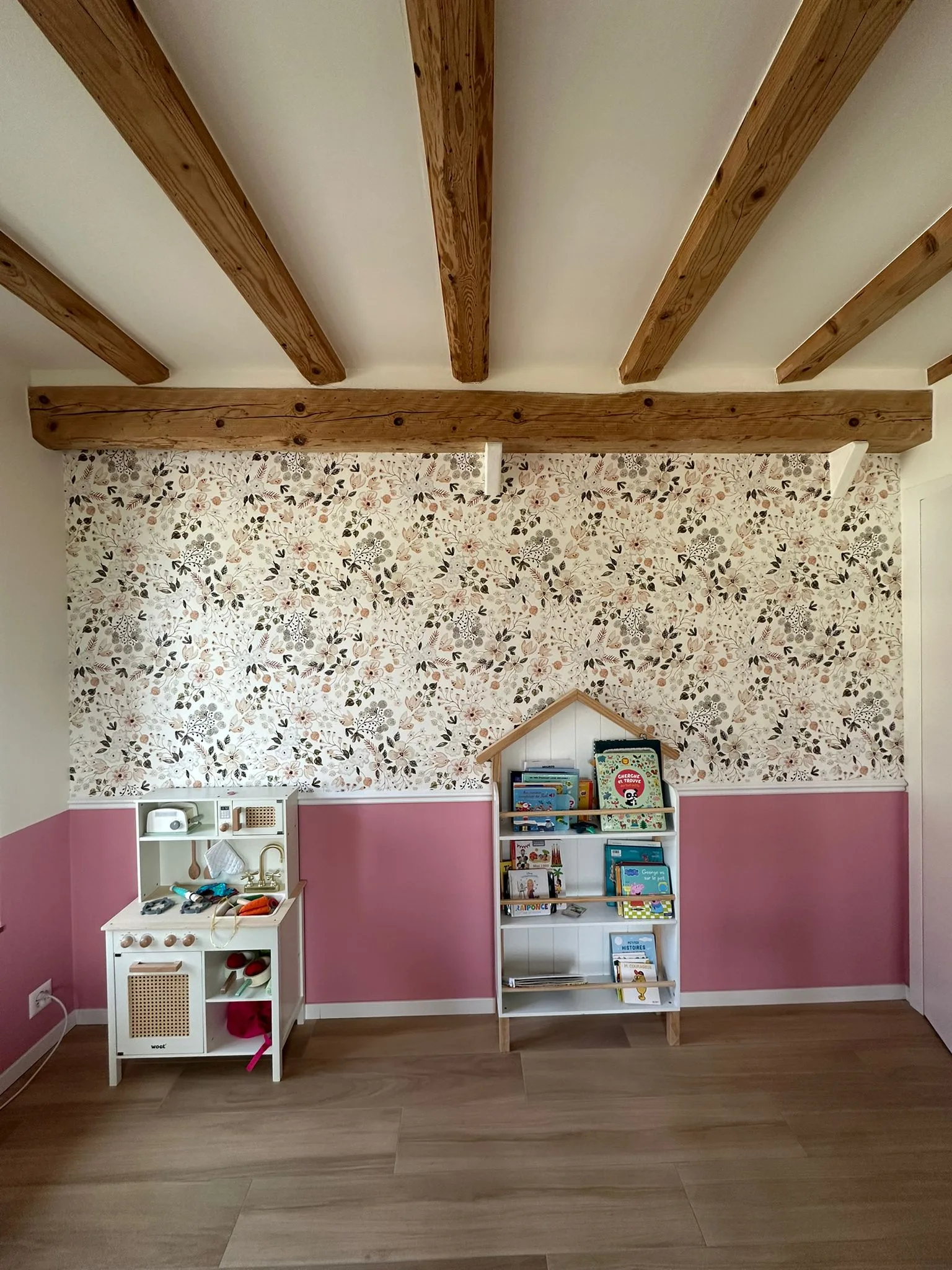 Chambre d'enfant à Genève : mur en papier peint floral en partie haute, soubassement peint rose en partie basse, séparés par une cimaise (moulure) MDF blanche, sous poutres apparentes.