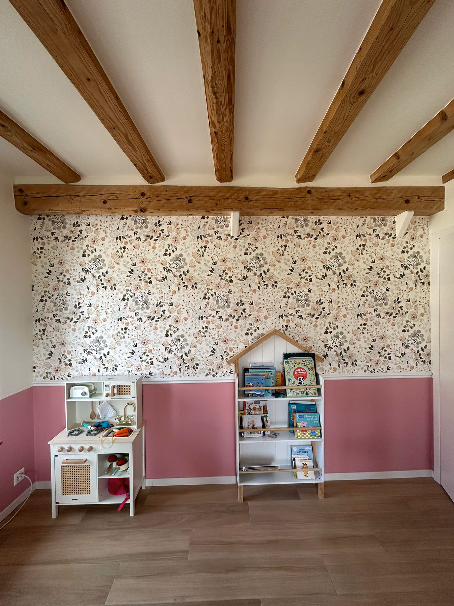 Chambre d'enfant à Genève : mur en papier peint floral en partie haute, soubassement peint rose en partie basse, séparés par une cimaise (moulure) MDF blanche, sous poutres apparentes.