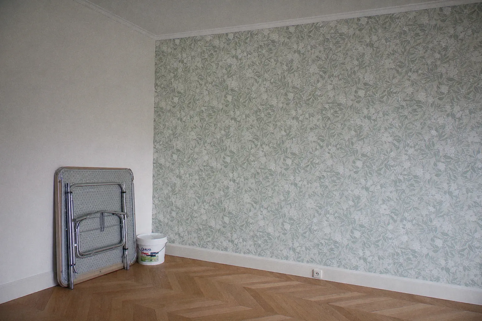 Mur d'accent fraîchement tendu d'un papier peint intissé à motif végétal, raccords nets, table à tapisser pliée et seau de colle en fin de chantier