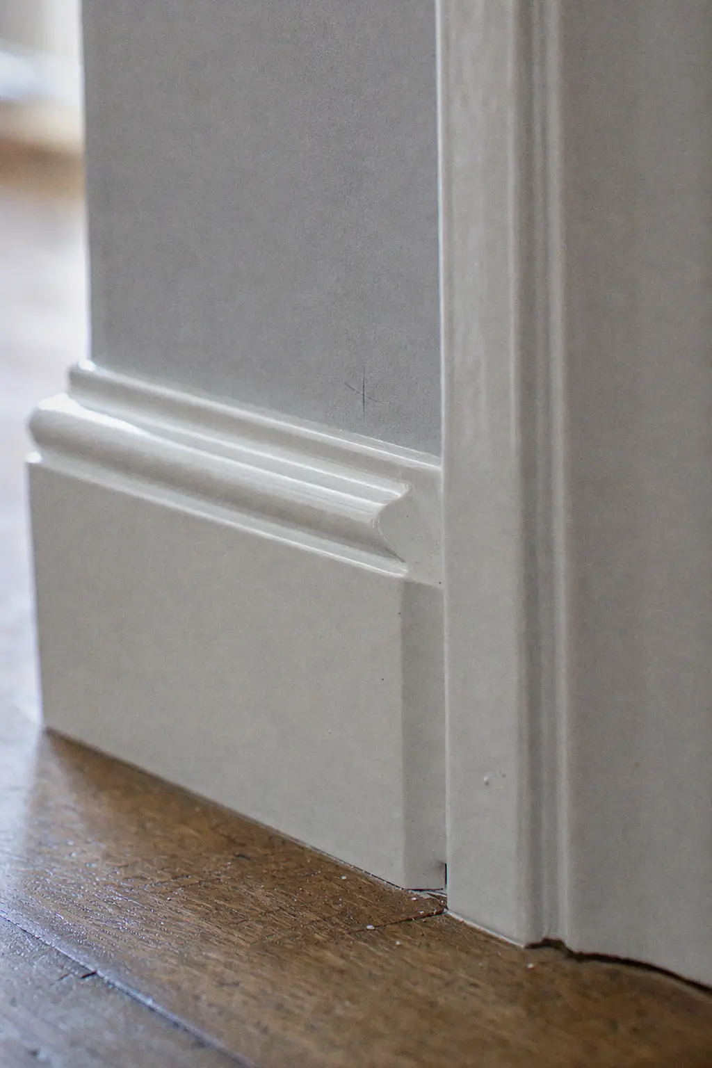 Plinthe et chambranle de porte en émail satiné blanc, arête nette contre le mur gris clair
