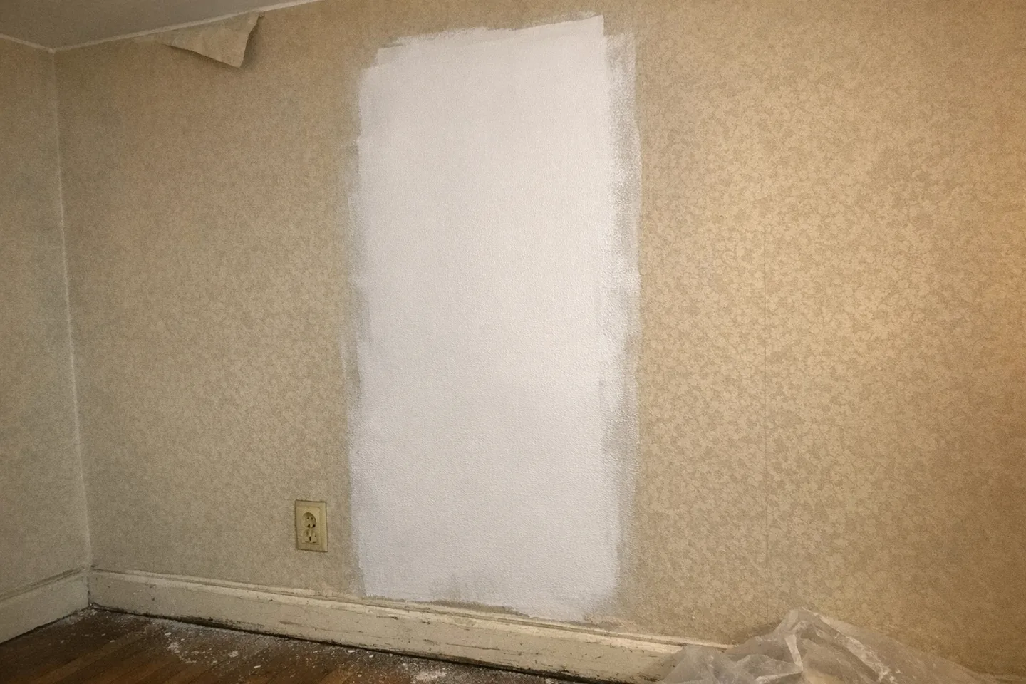 Mur d'appartement genevois où une bande de peinture blanche fraîchement passée au rouleau recouvre un vieux papier peint beige à motif discret, en lumière naturelle.